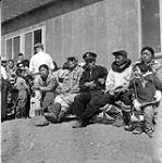 [Group of people sitting outside along the wall of a building, Niaqunngut, Iqaluit, Nunavut] 1960