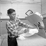 [Man [Elijah Nowdluk] using a clothes press, Iqaluit, Nunavut] 1960