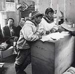 [Mathew and Henry Anatuk [Angnatuk] standing by a desk, Killiniq, Nunavut] 1960