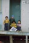 Young children on porch holding a print, Arviat 1979.