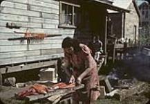 Une femme [Lillian Rose Brown] des Premières Nations traitant le saumon tandis que trois filles regardent [Ses noms Haida étaient Amgiidahl et Halthgoojewwhy] [1947]