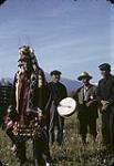 Four First Nations Elders, [pictured left to right: unidentified man, David Milton, George Milton, unidentified man] one wearing a button blanket and headdress, dancing while singing and playing the drum [at Kitwanga (Gitwangak), BC] [entre 1942 et 1959].