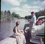 Un homme pêche dans le canal Rideau près d'Ottawa, une femme assise près de lui juin 1952