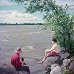 Man taking picture of woman on rocks in Brebeuf Park on the Ottawa River near Hull, Québec June 1952