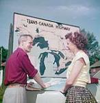 Two travellers - one man and one woman - consult a road map before the trans-Canada highway sign at the intersection of highways 15 and 17, Ottawa, Ontario July 1952