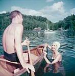 Un homme en canot et une femme avec un bonnet de bain nageant dans le lac Meech dans la région de Gatineau au Québec July 1952