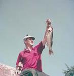 Man holding freshly caught fish, Nova Scotia. September 1953
