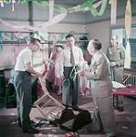 Four men and one woman in a messy room with streamers hanging from the ceiling  [Quatre hommes et une femme dans une pièce en désordre avec des serpentins pendant du plafond] 1954