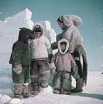 [An Inuk woman, possibly Naaktuuq, with from left to right, Michael Arvaaluk Kusugak, Paul Maniittuq, and Jose Kusugaq] An Inuk woman with three Inuit children outside dressed in winter clothing. October 1951.