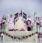 Three women in formal gowns and one in a black bathing outfit on a parade float, Midland août 1955
