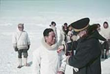 RCMP officer pins medal onto Inuk man's parka, outside in winter, Northwest Territories [Nunavut], 1957. 1957