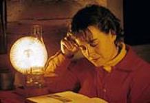 Jeune femme lisant à la lumière d'une lampe au kérosène. Chalet Shilly Shally, parc de la Gatineau n.d.