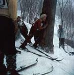 Jeune skieur appuyé contre un arbre avant son tour dans une compétition de saut en ski. Mini-ski (probablement Camp Fortune) n.d.