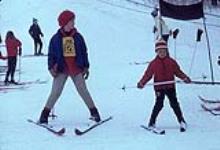 Female ski instructor teaching a young student. Midget Skiing (probably Camp Fortune) February, 1964