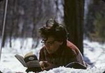 Helen Salkeld reading a novel in the snow [between 1955-1963]