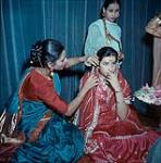 "Asian Evening" at Friendship House, Ottawa - Mrs. Azeez fixes 'bridal' costume of Zeba Hussain for a performance of a wedding scene; Mrs. Qureshi in background 1963