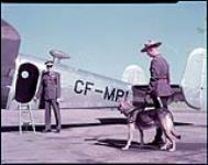 [RCMP const. B.A. Wright walking police dog "Rough" towards aircraft with Sgt. R. Ruhl, the pilot, waiting at the door.] août 1948.