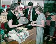 Tourists visiting the Clifton shops, Ottawa, examining hand-woven woolen fabrics shown by Miss M-L. Patterson. juin 1950.