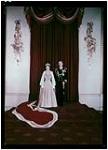 La reine Élisabeth II, portant une mante de fourrure blanche, une couronne et un sceau, se tient aux côtés du prince Philippe, duc d'Édimbourg, en uniforme [ca. 1950]