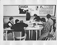 Students gathered around a table in a classroom [ca 1955-1976].