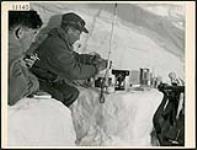 The Lovat Scouts, a Scottish regiment that played a prominent part in the invasion of Europe in WW II learned their mountain tactics and skiing from Canadian instructors high in the Rockies. Two Scouts hold up for the night in an ice cave, one is in bed his sleeping bag laid out on the snow shelf, his boots and parka forming a pillow, while the other prepares the evening meal, Jasper 1944