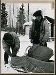 Deux hommes cris mettant des paquets dans un traîneau pour une expédition de trappage dans la forêt, au lac la Ronge March 1945