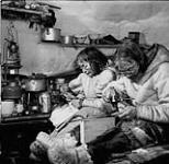 [Joseph Pork Kangiryuaq utilise un marteau et Hattie Niviaqsaaryuk coud à l'intérieur d'un igloo] Homme et femme Inuits assis dans un igloo. La femme coud et l'homme manipule un marteau n.d.