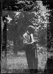 Man standing in grass in front of a wooded area [1925]