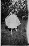 Fille tenant les côtés de sa robe, debout dans les hautes herbes [1925]