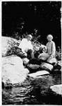 Man and woman sitting on rocks, next to water [1925]