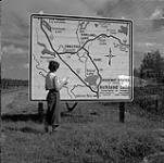 Et maintenant, où allons-nous? Audrey James debout à un grand panneau sur la route transcanadienne près de Kirkland Lake (Ontario) July 31, 1954.