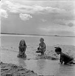 Enfants construisant un barrage avec du sable, Swan River, Manitoba June 23, 1956.