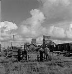 Men standing by grain elevators, Swan River, Manitoba 23 juin 1956.