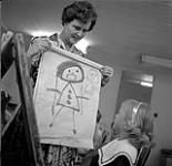 Teacher Jackie Otis holding a girl's painting during an art class, Calgary Allied Arts Centre août 1962.