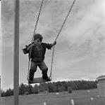 Boy standing on a swing, Swan River, Manitoba June 23, 1956.