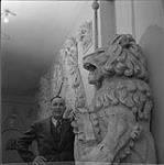 William Oosterhoff posing with masks and sculpture [ca 1954-1963].