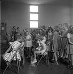 Schoolchildren sitting and standing in rows indoors [ca1954-1963]
