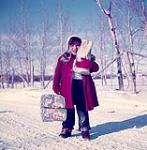 Jeune fille transportant des sacs d'épicerie sur une route enneigée à Buffalo Narrows (Saskatchewan) mars 1955