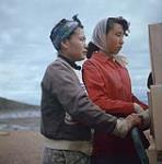Femmes participant au déchargement d'une barge de la Compagnie de la Baie d'Hudson à Apex, baie Frobisher, T.N.-O., [Iqaluit (anciennement baie Frobisher), Nunavut] [entre juin-septembre 1960].