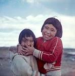 Portrait en gros plan de deux filles inuites [à droite: Martha Kalinovits (nee Lucasie) portant un chandail rouge] en train de jouer à Iqaluit (Nunavut). L'une s'amuse avec le visage de l'autre. [between June-September 1960].