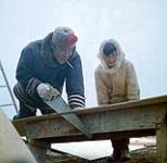 Deux Inuits construisent une structure en bois. Un des hommes utilise une scie à main. Arctique/Nord canadien [entre 17 juin-31 octobre, 1960].