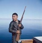 Sarpinak holding a rifle, Frobisher Bay, N.W.T., [Iqaluit (formerly Frobisher Bay), Nunavut] [between 16-19 August 1960].