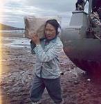 Femme déchargeant un sac de sucre d'une barge de la Compagnie de la Baie d'Hudson à Apex, baie Frobisher, T.N.-O., [Iqaluit (anciennement baie Frobisher), Nunavut] [between June-September, 1960].