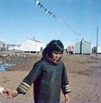 Young girl walking and holding hands with someone. Arctic / Northern Canada [entre 17 juin-31 octobre, 1960].