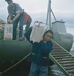 Fille déchargeant un sac de sucre d'une barge de la Compagnie de la Baie d'Hudson à Apex, baie Frobisher, T.N.-O., [Iqaluit (anciennement baie Frobisher), Nunavut] [between June-September, 1960].