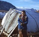 Woman standing outdoors in front of stretched sealskin. Arctic / Northern Canada [entre 17 juin-31 octobre, 1960].