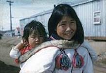 Fille portant sa petite soeur dans le parka de sa mère, Iqaluit, Nunavut [Napatchie portant Paujungi]  [between June-September, 1960].