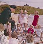 Le commandant du navire "Christmas Seal", Peter Troake raconte des histoires aux enfants alors qu'ils attendent pour passer des rayons-x, Terre-Neuve août 1960