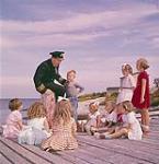 Le commandant du navire "Christmas Seal", Peter Troake raconte des histoires aux enfants alors qu'ils attendent pour passer des rayons-x, Terre-Neuve août 1960