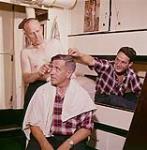 Le capitaine Peter Troake coupe les cheveux de Ches Pelley, sous les yeux de Gerald Drover, à bord du "Christmas Seal". Terre-Neuve. August 1960